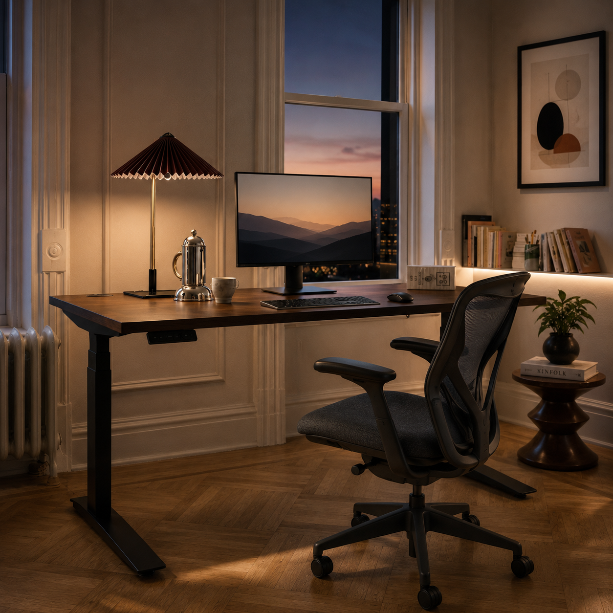 Walnut standing desk at dusk with a monitor showing mountains and a warm table lamp